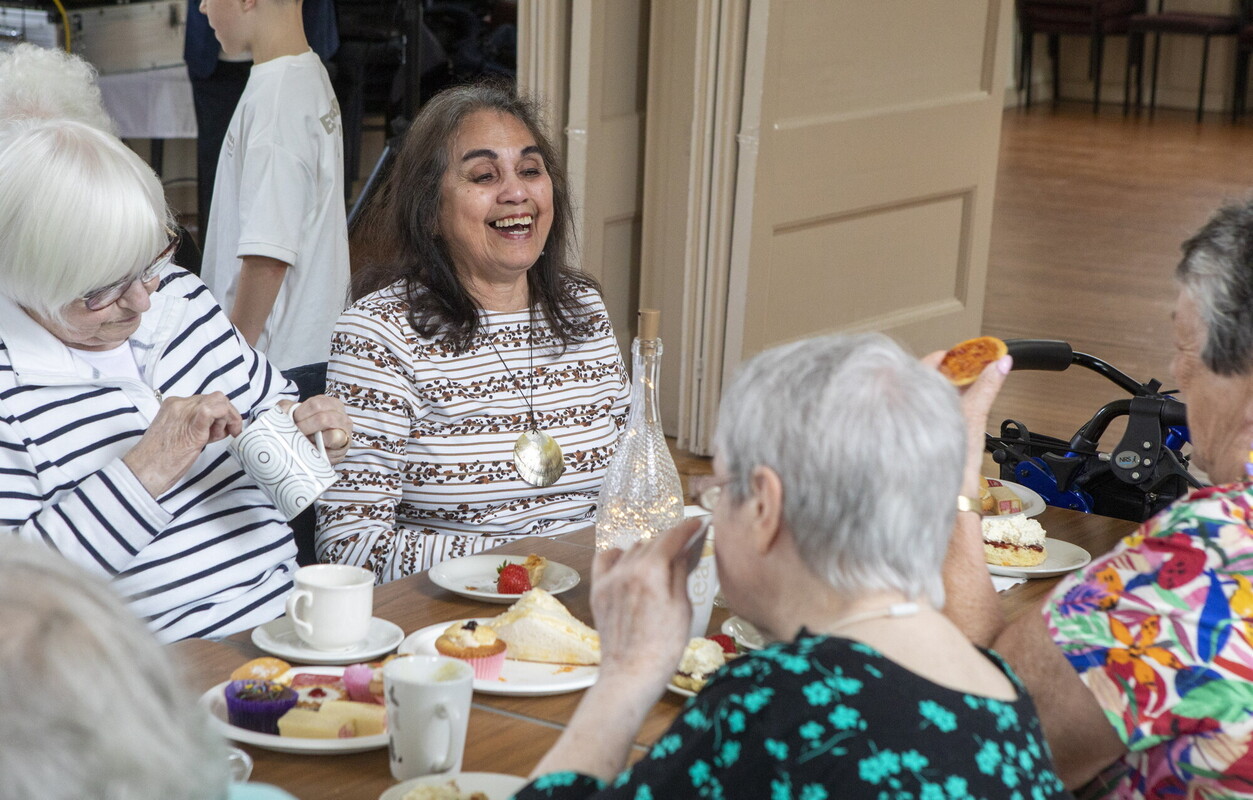 A group of people laughing at a table filled with food and drinks