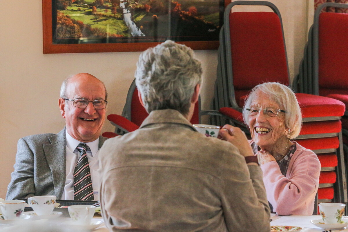 A group of people laughing while sat at a table with cups and saucers