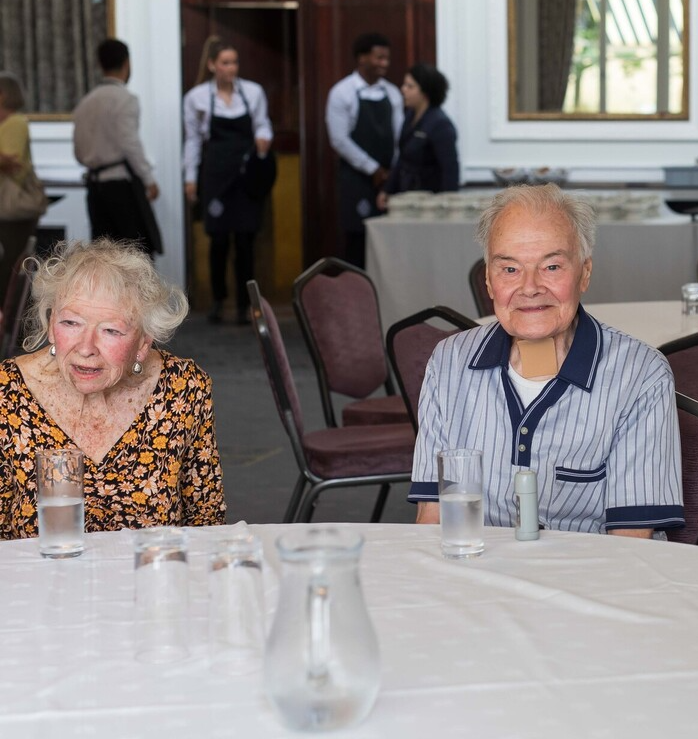 Two people smiling while sat at a table with glasses of water